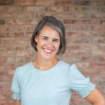 Author Katie Reid standing in front of a brick wall with her hand on her hip.