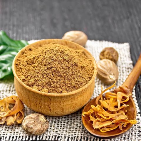 Wooden bowl filled with the ground spice, mace. Mace pods surround the bowl.