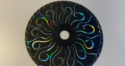 Image of a CD that has been covered in black. Some of the coating has been scratched off in a swirly design to reveal the shiny underneath. 