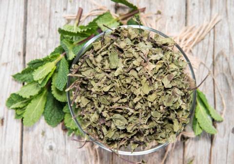 Image of a bowl of dried mint leaves on a wooden plank table.