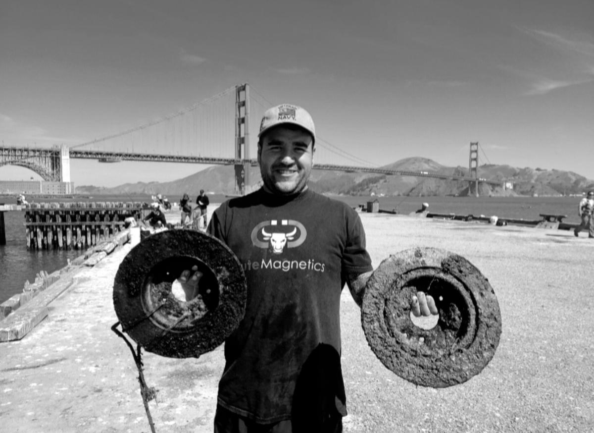 Image of a man holding metal objects while standing in front of bridge.