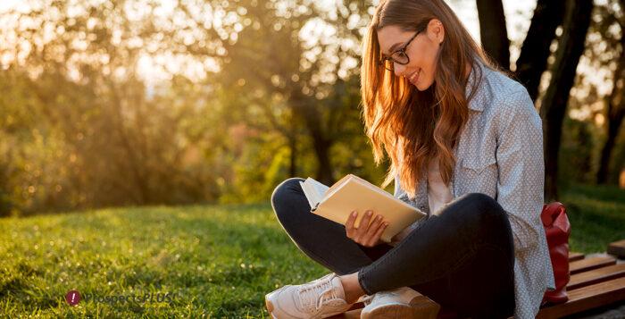 Image of woman reading outside, sitting under a tree with the sunlight fading.