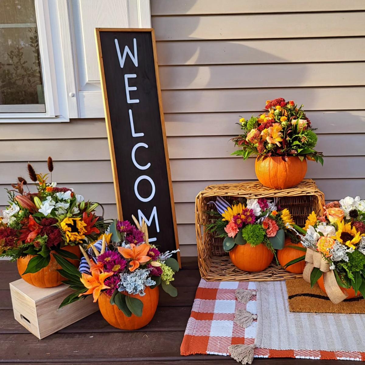 Pumpkins filled with Fall floral arrangements on front porch with welcome sign.