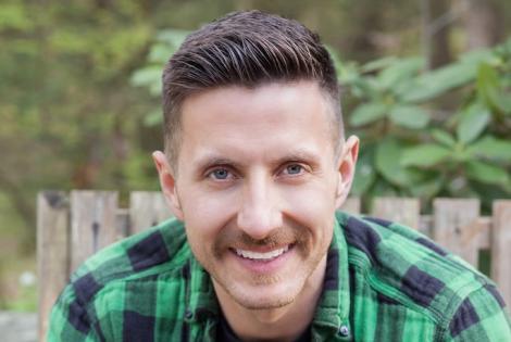 Image of Dominic Thrasher. A man with short brown hair and a mustache. He is wearing a green and black plaid shirt and smiling.